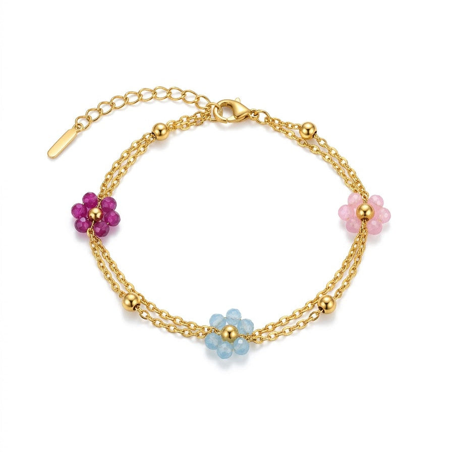 A gold double-strand chain bracelet with three flower charms in pink, purple, and light blue, displayed on a clean white background.
