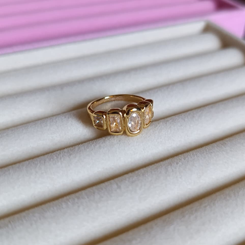 Gold ring with multiple gemstones on a white and pink striped surface