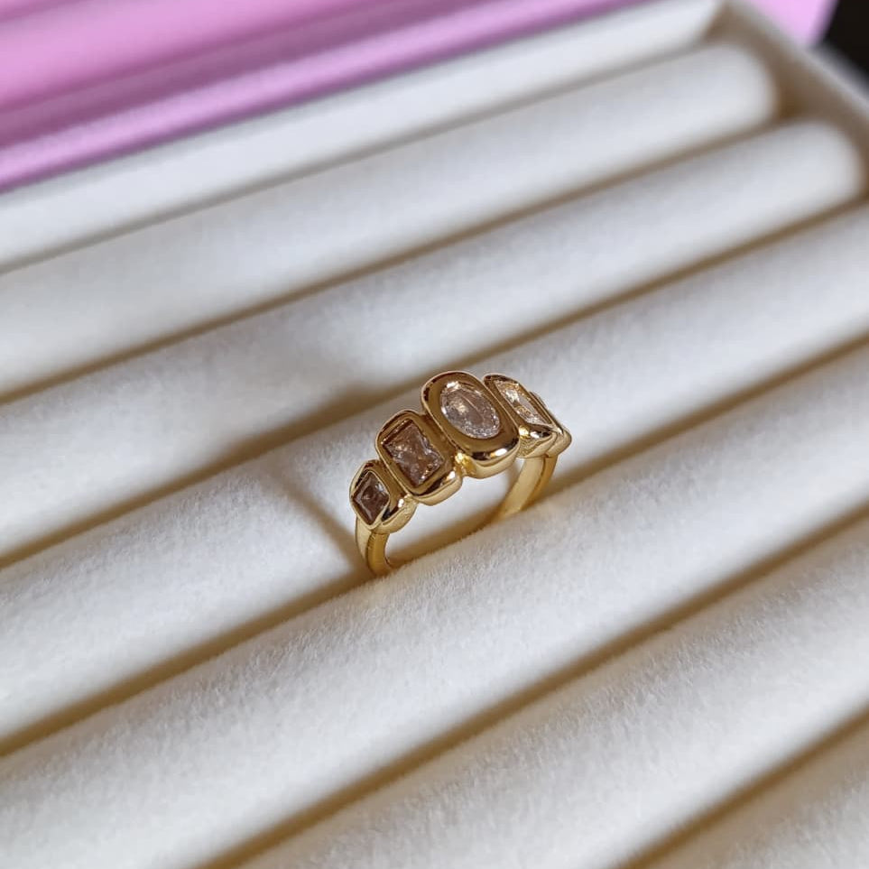 Gold ring with three large gemstones on a white jewelry display box.