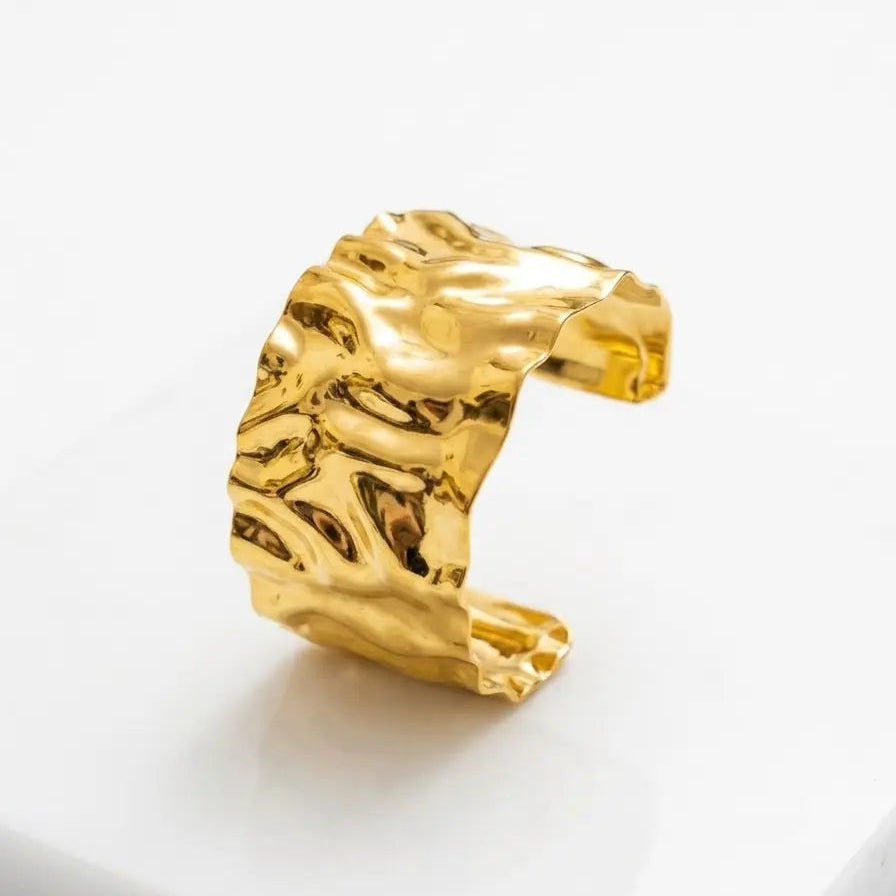 A textured, wavy open cuff bracelet in polished yellow gold, displayed on a clean white surface.