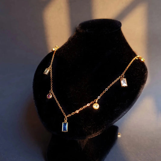 Gold necklace with gemstones on a black velvet stand against a neutral background